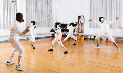 Coaches demonstrating to young athletes attack movements with rapier during fencing workout