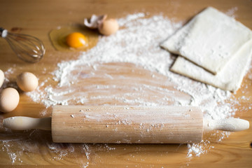 Baking ingredients. Bowl, eggs, flour, egg cattle, rolling pin and egg shell on a wooden board on top.