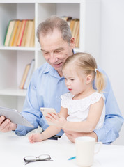Little girl uses the application on the phone, and an elderly man works on tablet computer at home