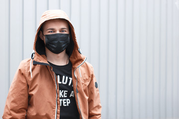 Stylish young man in black face mask on grey background. Coronavirus quarantine situation. Street...