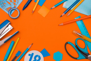 Back to school concept flat lay.Blue rulers,color pencils,pens,felt pen,scissors,stapler,sticky tape,copybook and plastic geometric elements on the orange background.Copy space for text,top view