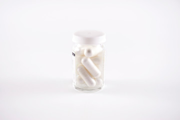 Glass pill bottle full with white capsules (frog eye view on white background)