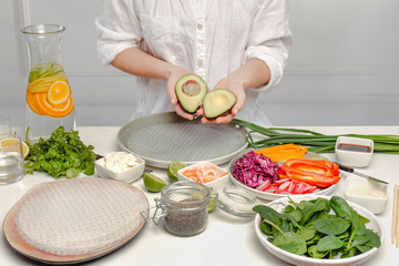 Side view of woman in a white shirt holding avocado halves, in the process of making spring roll.