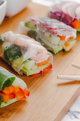 Delicious asian dish. Side view of fresh spring rolls with shrimp and vegetables and different sauces served on a wood plate with chop sticks.