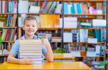 Single dreaming boy at the desk in the library enjoy books. European boy explore books. Pupil loves lecture, education, preparing for school.