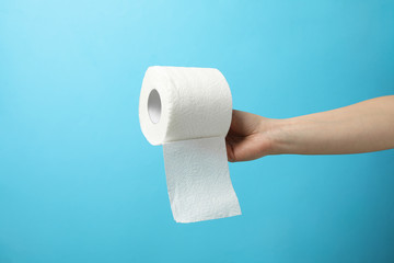 Hand holds roll of toilet paper on blue background