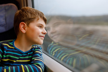 Adorable kid boy traveling by train. Happy smiling child looking out of the window during train...