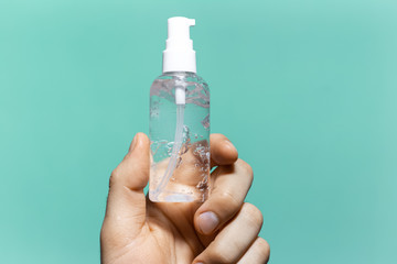 Close-up of male hand holding small plastic bottle of sanitizer antibacterial gel on background of cyan aqua menthe color.