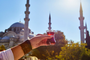 A cup (armud) of traditional Turkish tea in hand against the background of a mosque in Istanbul