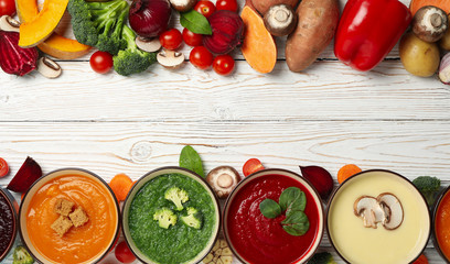 Vegetable soups and ingredients on white wooden background, top view