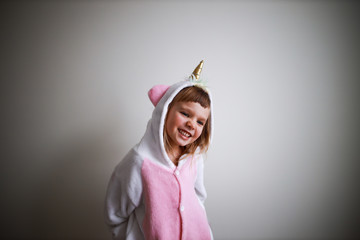 little girl smiling in a unicorn cosume on white wall background