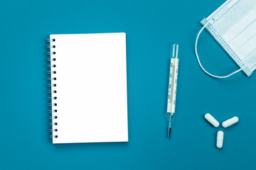 Coronavirus. Notebook copy space, medical mask, thermometer and tablets on a colored background.
