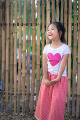 Portrait of happy asian little girl standing in the park with bamboo wall