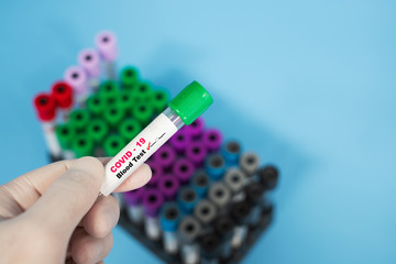 Cropped Hand Of Person Holding Covid-19 or Coronavirus Test Tube Over Blue Background