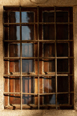 Closeup of an old window with wrought iron security bars and wooden shutters on a stone wall. Tuscany, Italy, Europe