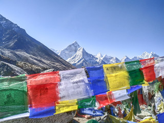 Colorful buddhist prayer flags waving in the Himalayas. Clear blue sky. Selective focus. Blurred Ama Dablam mountain is visible in the background.