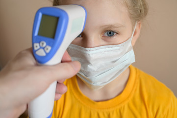 Little girl wearing protective medical mask. Temperature measurement by infrared thermometer.