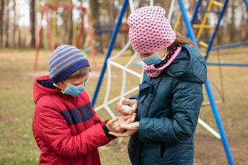 Small girl and boy using hand sanitizer while playing on playground. Hands disinfection during coronavirus epidemic