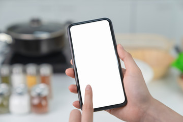 Hand holding blank screen of smartphone at home in kitchen. for graphic display montage.