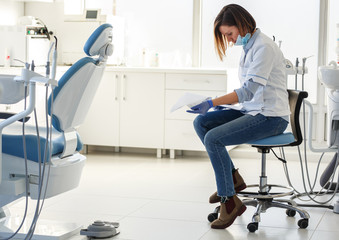 Female dentist in dental office .She tired after hard work, sitting on chair and planing list of...