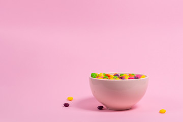 Bowl full of color candies on pink background