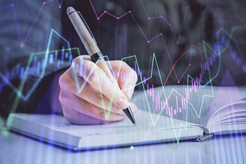 Double exposure of woman's hands making notes with forex graph hologram. Concept technical analysis.