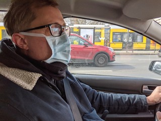 Man with face mask driving in car through city