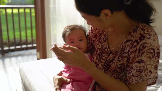asian mother holding a sleepy baby girl while sitting in front of the door