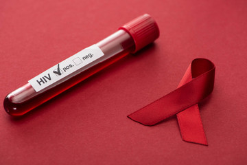 red awareness aids ribbon and positive hiv blood sample test on red background - obrazy, fototapety, plakaty