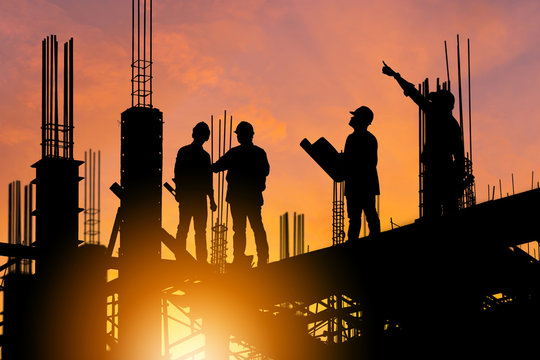 Silhouette of Engineer and worker on building site, construction site at sunset in evening time.