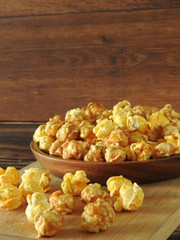 Front view of delicious popcorn in round wooden plate isolated on wooden background. Include buttery caramel corn and rich cheddar cheese corn. Food and snack concept. With copy space.