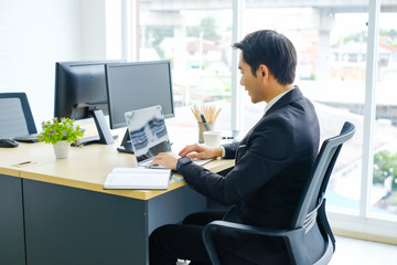 Side view of Young businessman sitting and working on desk and using smart phone connecting internet and documents at office, employee or company ceo using online apps software at workplace