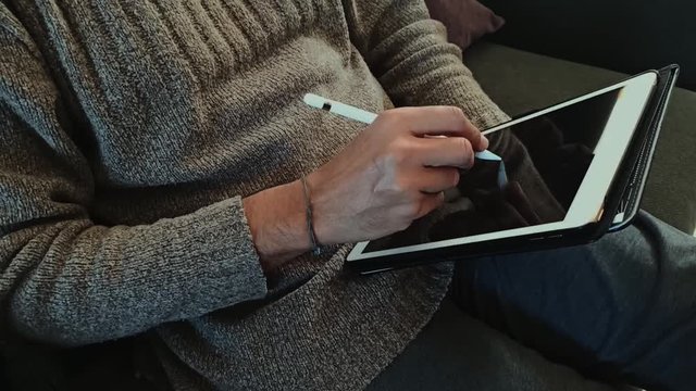 Uomo in abbigliamento casual che disegna al tablet a casa seduto sul divano