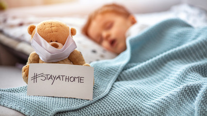 Child in home quarantine at the bed, sleeping, with medical mask on his sick teddy bear, for...