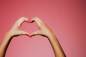 Woman's hands with bright manicure isolated on pink background love sign