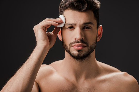 handsome nude man using cosmetic cotton pad isolated on black