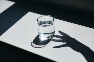 Water glass with strong shadows and hand gesture silhouette on white background