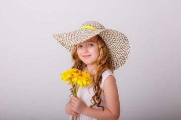 a little blonde girl in a straw hat with a bunch of yellow flowers in her hands on a white background