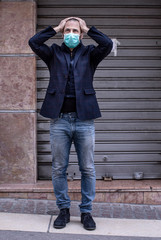 Manager con mascherina e giacca e jeans sconsolato di fronte alla serranda chiusa della sua attività, , si porta le mani alla testa