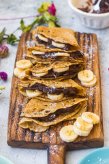 French delicious ruddy crepes - thin fried sweet pancakes stuffed with chocolate hazelnut paste, bananas. Folded crepes, pancakes on wooden board.