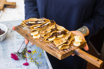 Woman holds delicious french chocolate crepes - thin fried sweet folded pancakes stuffed with bananas and paste. Homemade. Wooden board