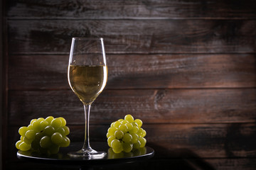 Fototapeta premium White wine glass with grapes on a table on a wooden background