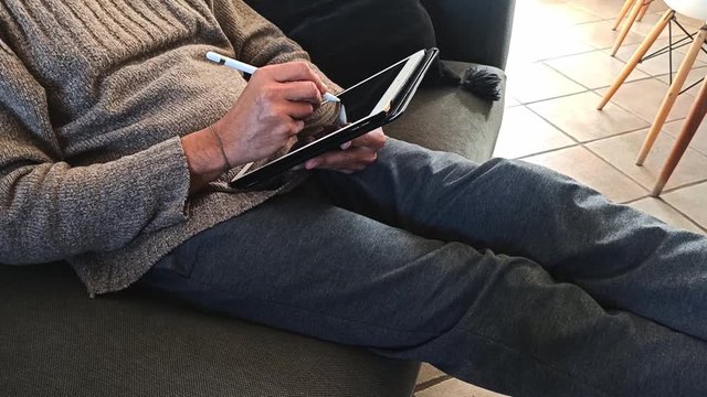 Uomo in abbigliamento casual che disegna al tablet a casa seduto sul divano