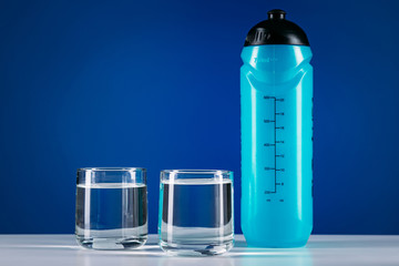 Closeup blue sport water bottle and two glasses isolated on blue background
