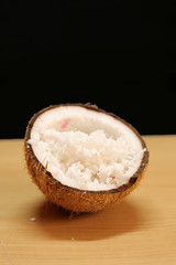 Coconuts with coconut flakes are isolated on a wooden table on a black background