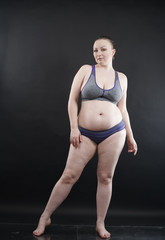 Obraz premium plus size woman shows her body in stretch marks and hair with cellulite and encourages you to love and accept yourself in any way . black background in the Studio. full- length photo.
