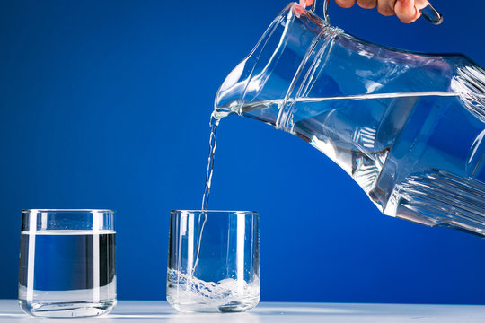 Hand pours water from jug into a glass isolated blue background