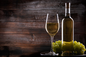 White full wine bottle and wineglass with grapes on a table on a wooden background