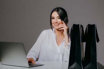 Smiling girl in a white shirt, with a laptop, and holding a credit card and a phone, preparing for...