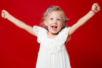 Happy young blonde curly model girl smiling jumping in white dress isolated on red